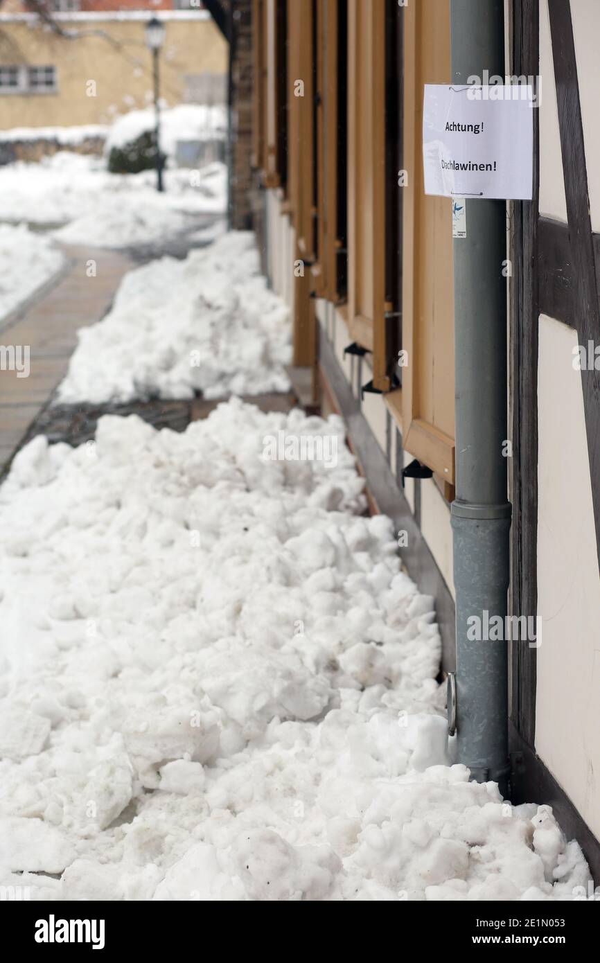 Wernigerode, Deutschland. Januar 2021. Schnee liegt auf den Dächern von Häusern. Mit dem Einsetzen des Tauwetters besteht die Gefahr fallender Schneemassen, auch Dachlawinen genannt. Hausbesitzer verwenden Schilder, um die vorbeifahrenden Menschen auf die Gefahr aufmerksam zu machen. Quelle: Matthias Bein/dpa-Zentralbild/ZB/dpa/Alamy Live News Stockfoto