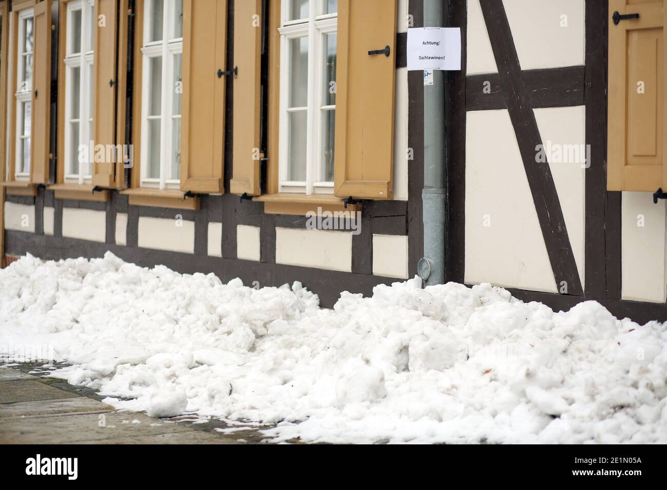 Wernigerode, Deutschland. Januar 2021. Schnee liegt auf den Dächern von Häusern. Mit dem Einsetzen des Tauwetters besteht die Gefahr fallender Schneemassen, auch Dachlawinen genannt. Hausbesitzer verwenden Schilder, um die vorbeifahrenden Menschen auf die Gefahr aufmerksam zu machen. Quelle: Matthias Bein/dpa-Zentralbild/ZB/dpa/Alamy Live News Stockfoto