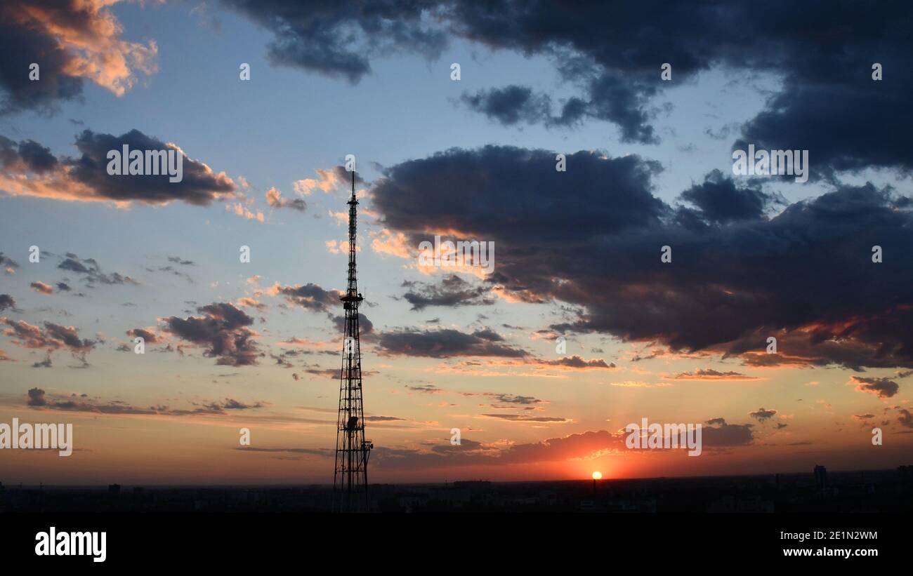 Wolkenlandschaft mit Industriekommunikationsturm und dunkelvioletten Wolken, während goldene Sonnenstrahlen durchscheinen. Rote Sonne Wolkenlandschaft des Sonnenuntergangs. Düsteres Drama Stockfoto