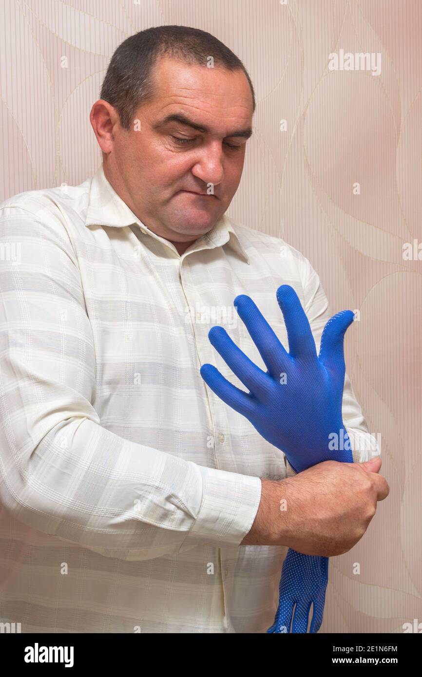Der kaukasische Mann legt einen blauen Stoffhandschuh auf die Hand, bereitet sich auf die Arbeit vor. Handschutzkonzept, Gesundheitsschutz. Stockfoto