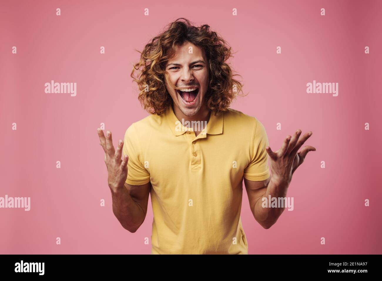 Portrait eines jungen wütenden Mannes, der schreit und anschaut Kamera über rosa Hintergrund Stockfoto