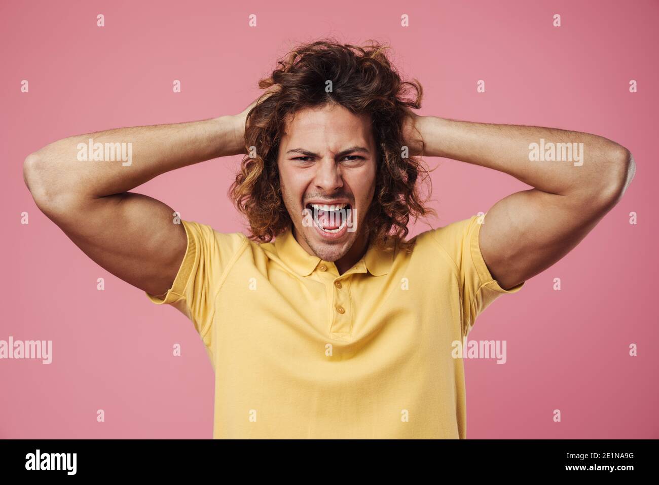 Portrait eines jungen wütenden Mannes, der schreit und anschaut Kamera über rosa Hintergrund Stockfoto