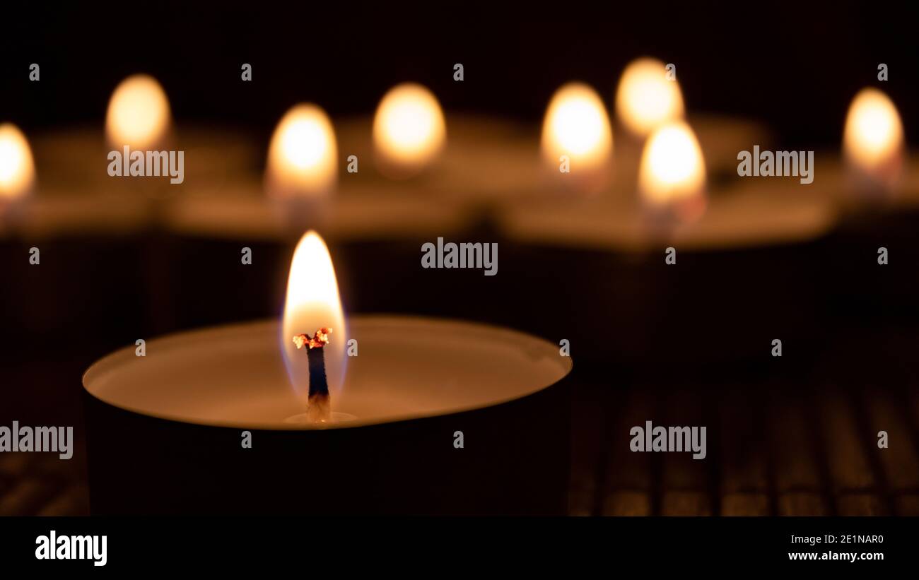 Nahaufnahme brennender Kerzen im Dunkeln mit acht verschwommenen Kerzen im Backgorund. Abstrakt Kerzen Hintergrund Stockfoto