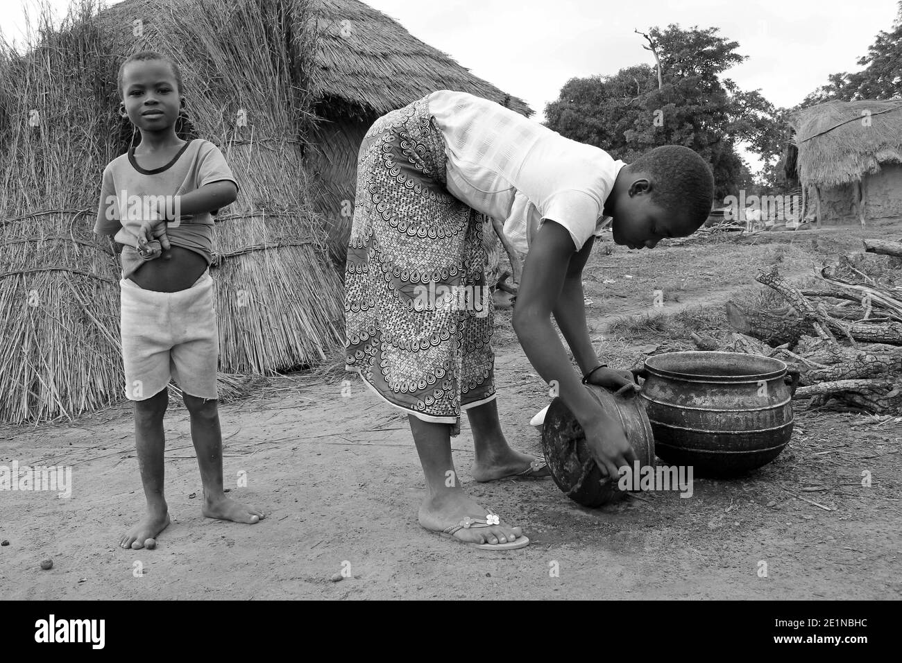 Ghanaische Mädchen der Gonja Tribe Scrubbing Kochtopf während Der Jüngere Bruder Steht Vor Der Kamera Stockfoto