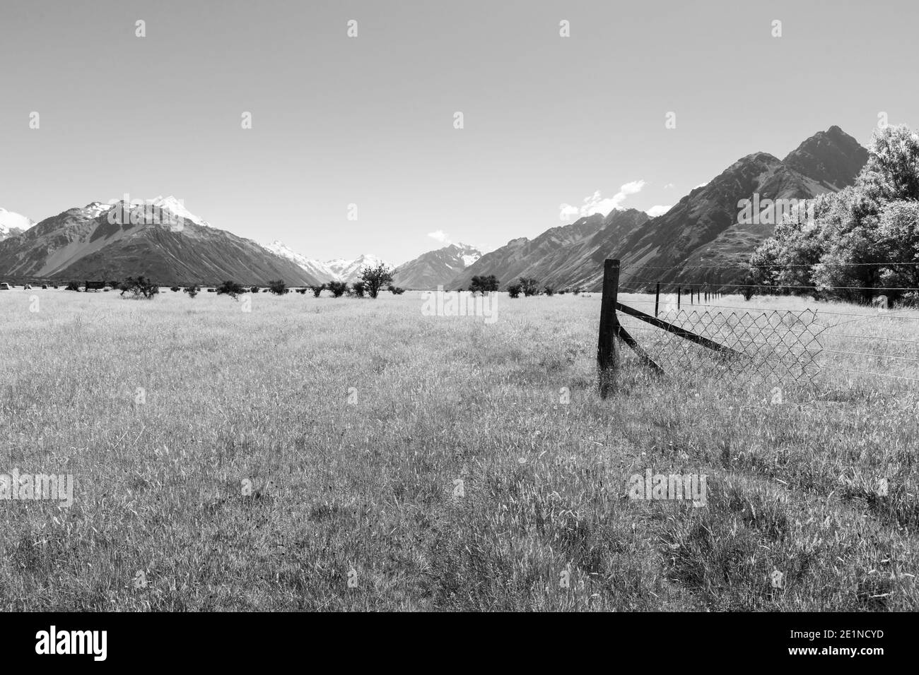 Monochromes, flaches Ackerland mit Zaun zwischen den Bergen der Soutern Alpen auf einer der tollen Wanderungen Neuseelands. Stockfoto