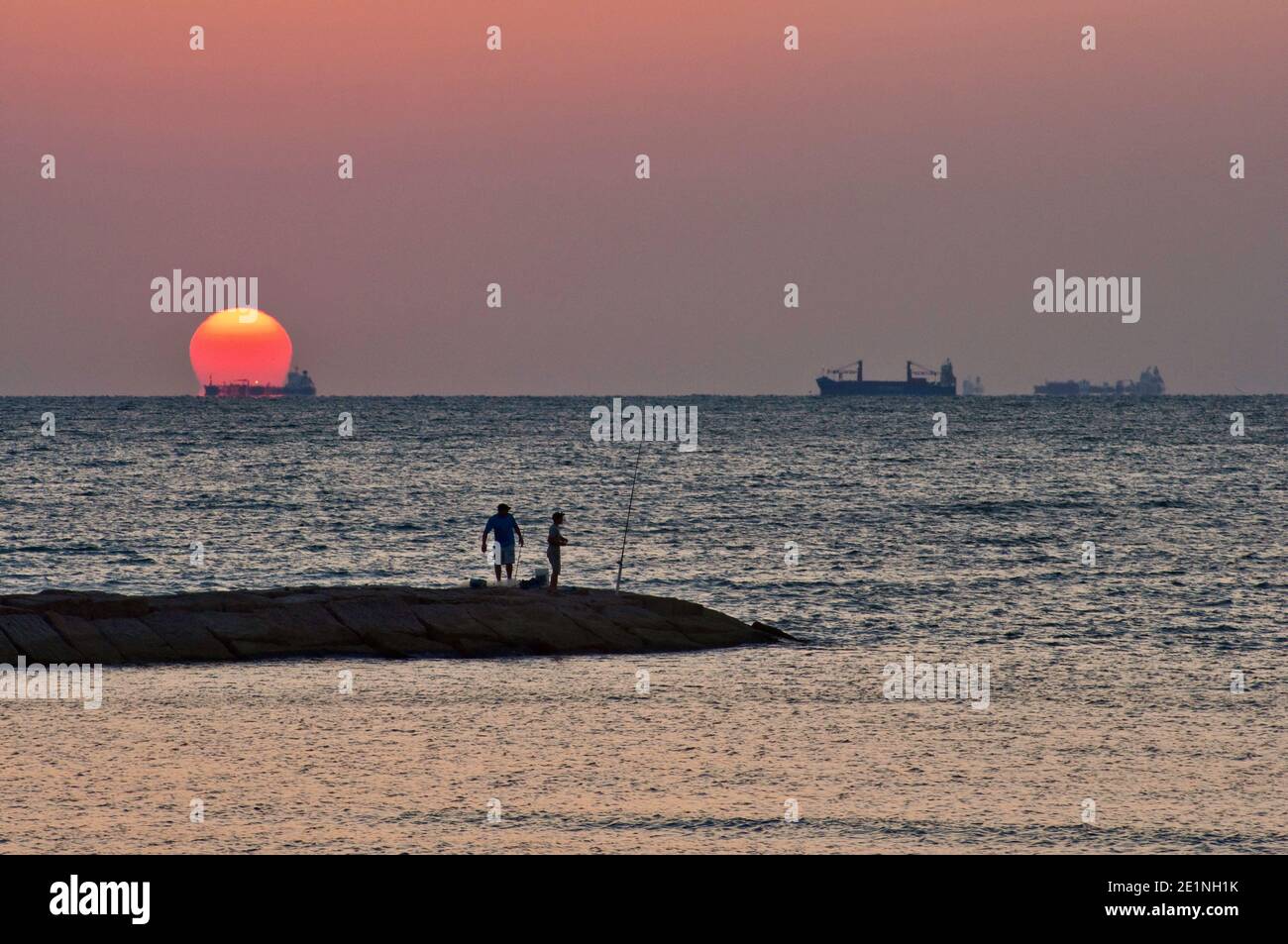 Männer, die am Seawall Boulevard Pier angeln, Schiffe auf dem Weg zum Hafen, bei Sonnenaufgang in Galveston, Texas, USA Stockfoto