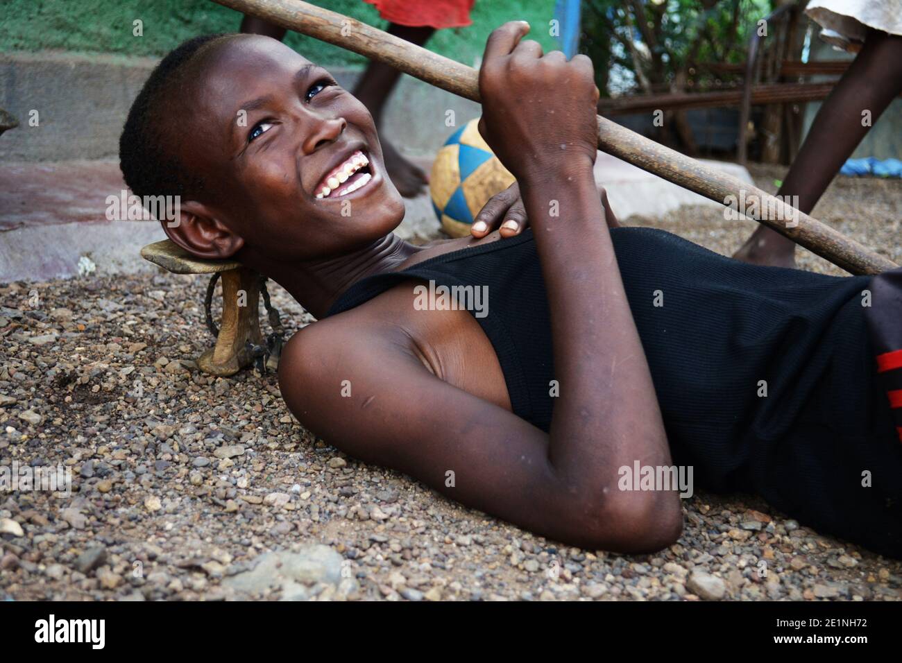 Porträt eines kenianischen Jungen aus dem Stamm der Turkana, der mit einem Stock und einem Kopfstand posiert, der von lokalen Pastoralisten verwendet wird. Aufgenommen in Kakuma in Kenia. Stockfoto