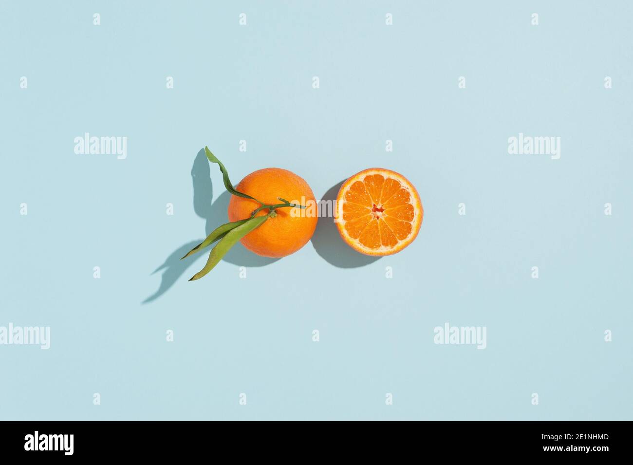 Kreativer Hintergrund mit frischen orangenen Mandarinen auf blauem Hintergrund. Bild mit harten Schatten. Abstrakter Sommer- oder Winterhintergrund. Stockfoto