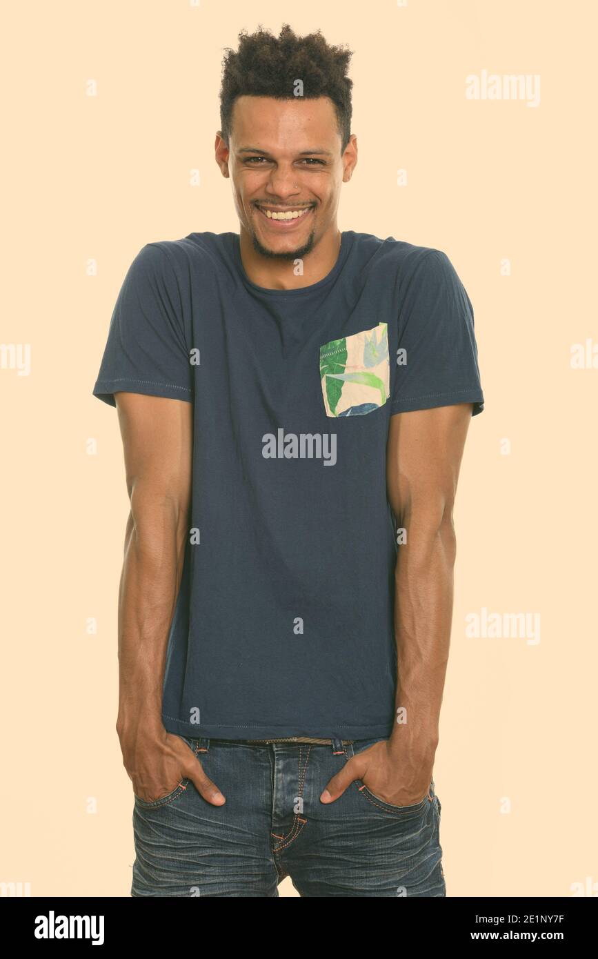 Studio shot junger afrikanischer Mann glücklich lächeln und lachen mit den Händen an den Taschen Stockfoto