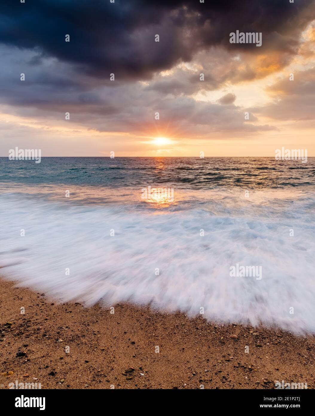 Ein farbenfroher Ocean Sunset Sky als sanfter Wave Rolls Shore in einem vertikalen Bildformat Stockfoto