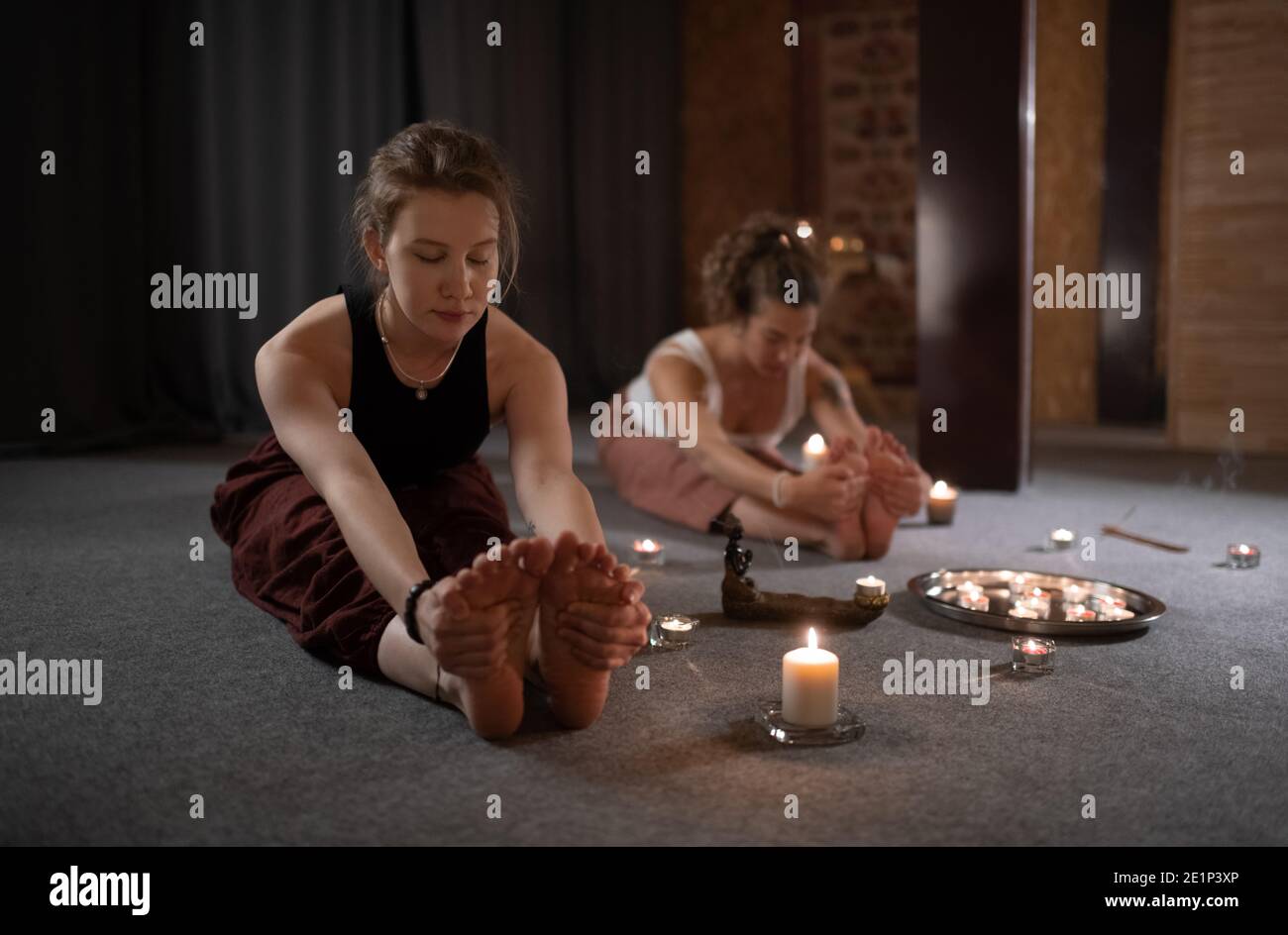 Schlank weiblich tun sitzend vorwärts Biegen Pose in der Nähe von Kerzen und Freund im Studio Stockfoto