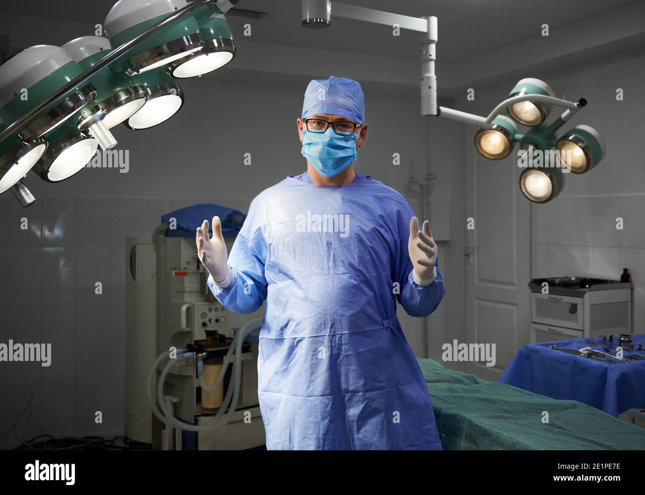 Porträt eines Chirurgen, der im Operationssaal des Krankenhauses auf die Kamera schaut. Mann Arzt trägt OP-Uniform, sterile Handschuhe, Gesichtsschutz, medizinische Kappe. Konzept der Medizin, Chirurgie Stockfoto