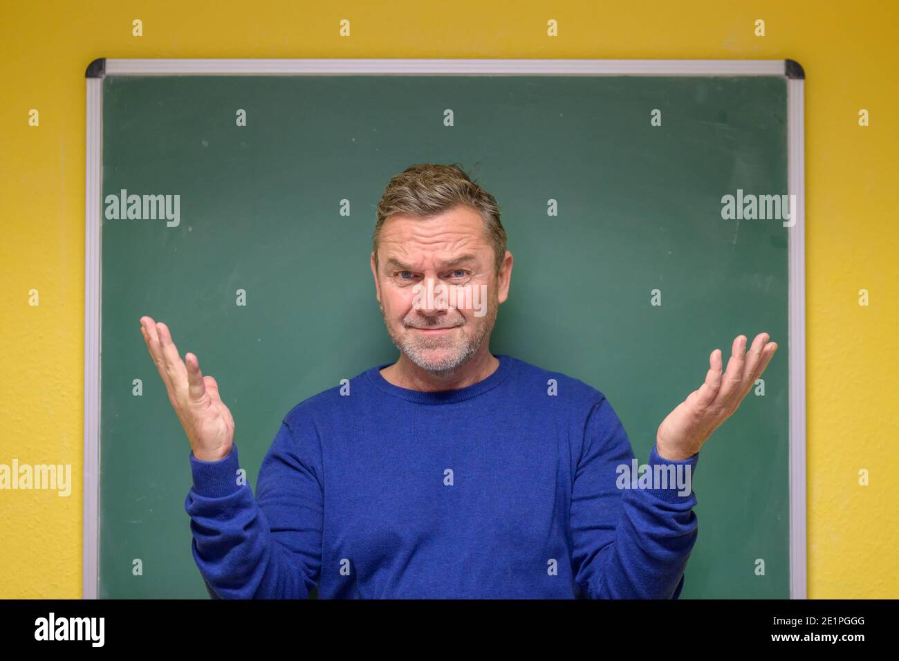 Männlicher Lehrer gestikuliert mit seinen Händen, während er innen steht Vorderseite einer kleinen Tafel an der Wand eines Schulungsraum Stockfoto