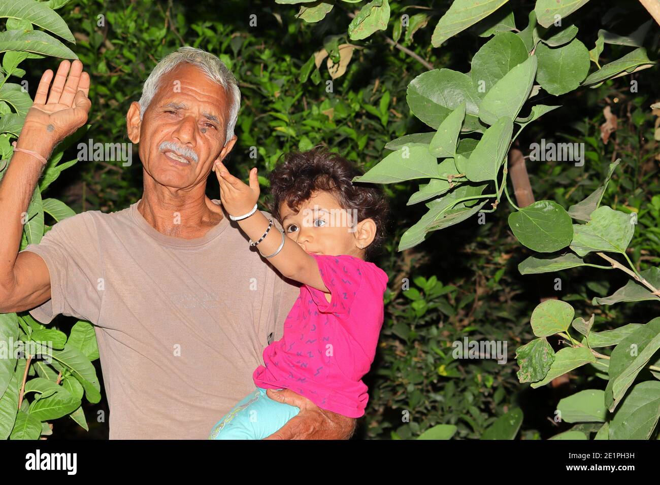 Ein schönes indisches Kind und Großvater lächeln im Garten und schauen auf die wachsende Schönheit der Bäume, indien Stockfoto