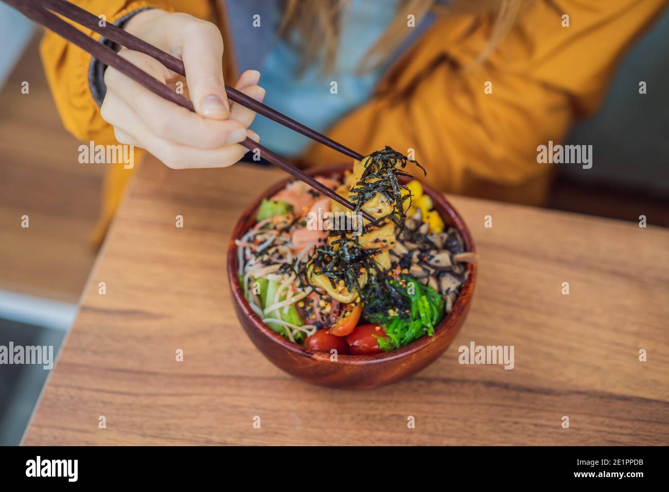 Frau, die rohe Bio-Poke-Schale mit Reis und Gemüse aus nächster Nähe auf dem Tisch isst. Draufsicht von oben horizontal Stockfoto