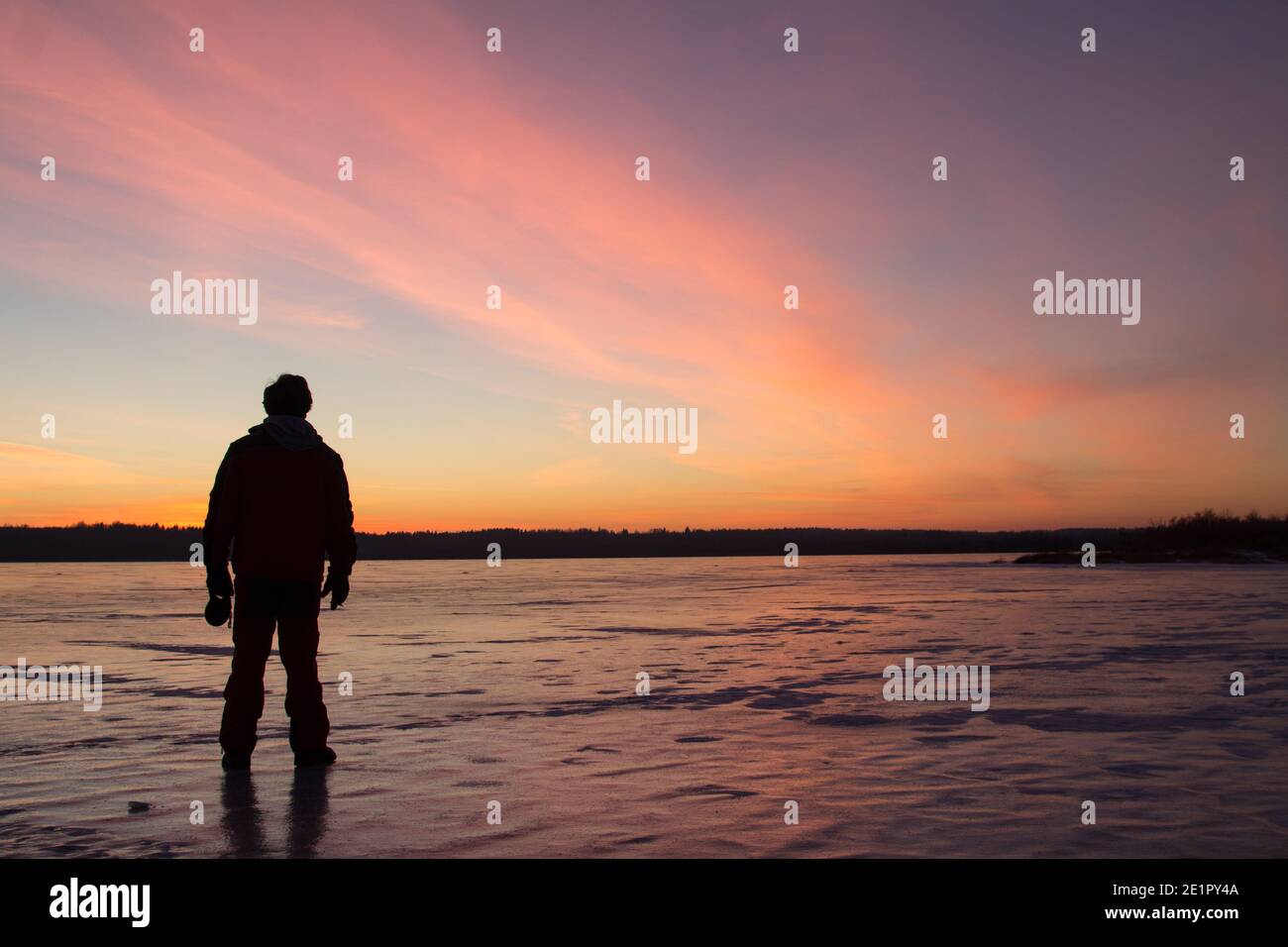 Silhouette eines Mannes bei Sonnenuntergang, der auf dem Eis eines gefrorenen Sees steht. Stockfoto