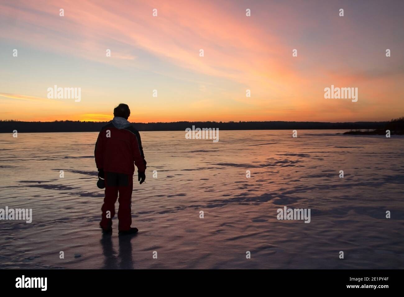Silhouette eines Mannes auf dem Hintergrund eines eisbedeckten Sees bei Sonnenuntergang. Stockfoto