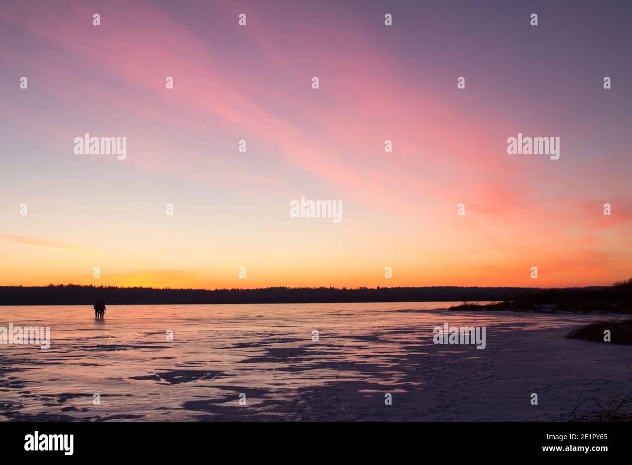 Zwei Silhouetten von Menschen vor dem Hintergrund des Sonnenuntergangs auf dem Eis eines gefrorenen Sees. Winterhintergrund. Stockfoto