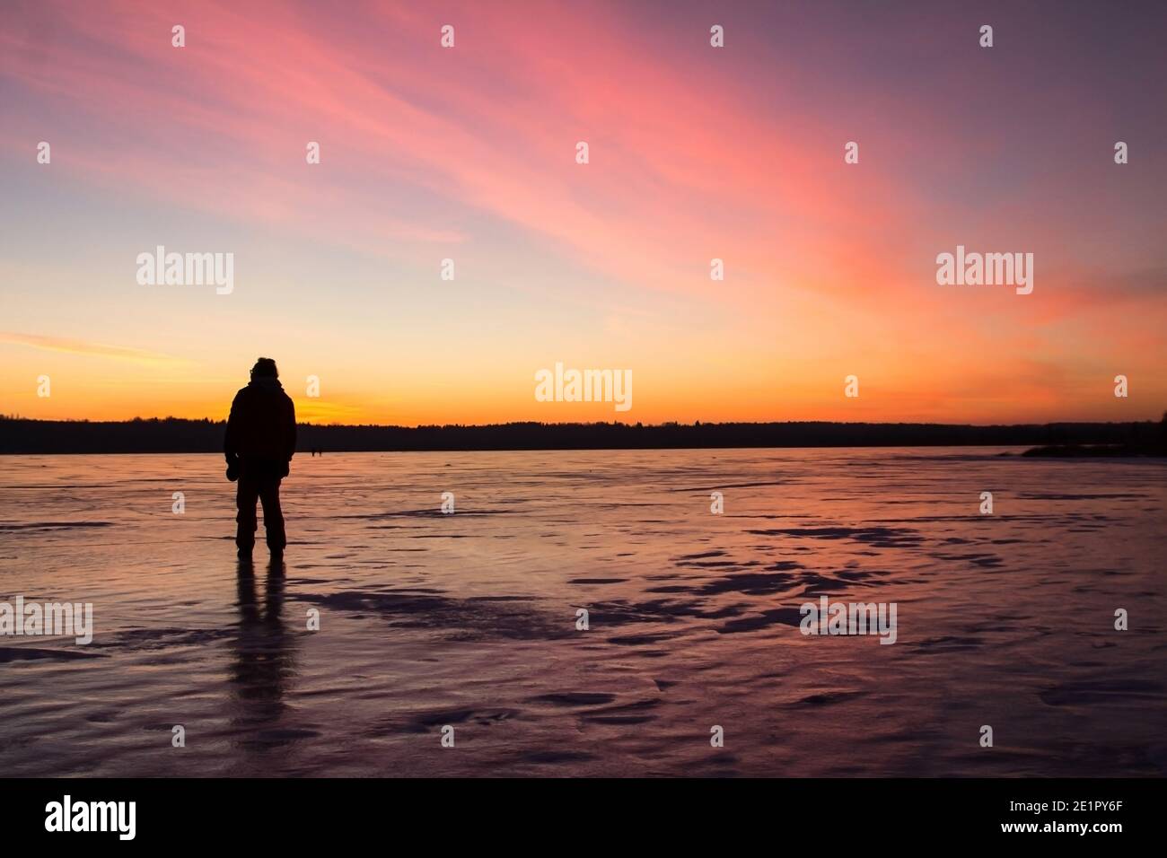 Die Silhouette eines Mannes, der im Licht des Sonnenuntergangs auf dem Eis eines gefrorenen Sees steht. Stockfoto