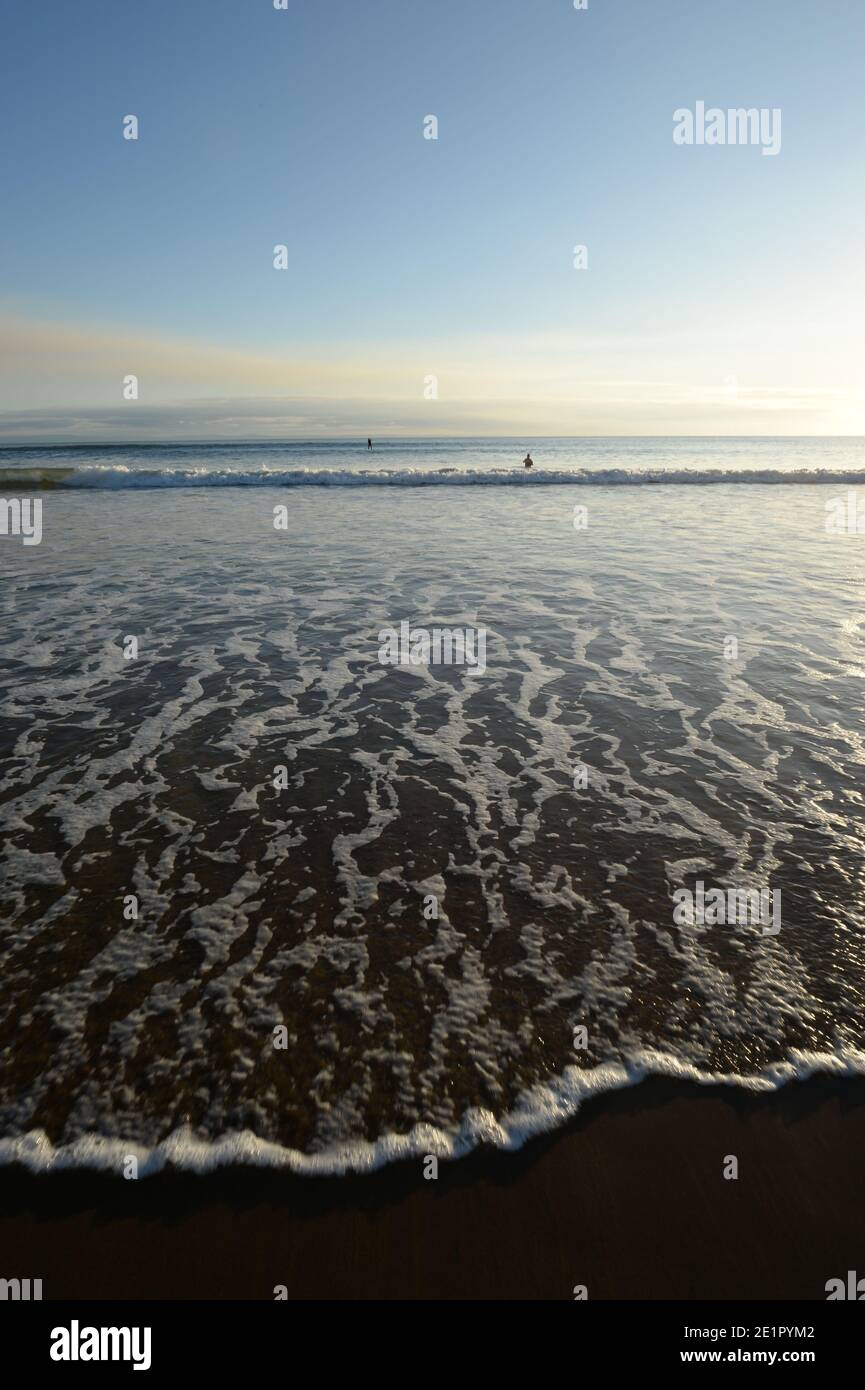 Kleine Wellen strömen den Strand hinauf bei der ankommenden Flut Den Sand beim Schwimmen in Spitzen-Mustern aus Schaum bedecken wade raus Stockfoto