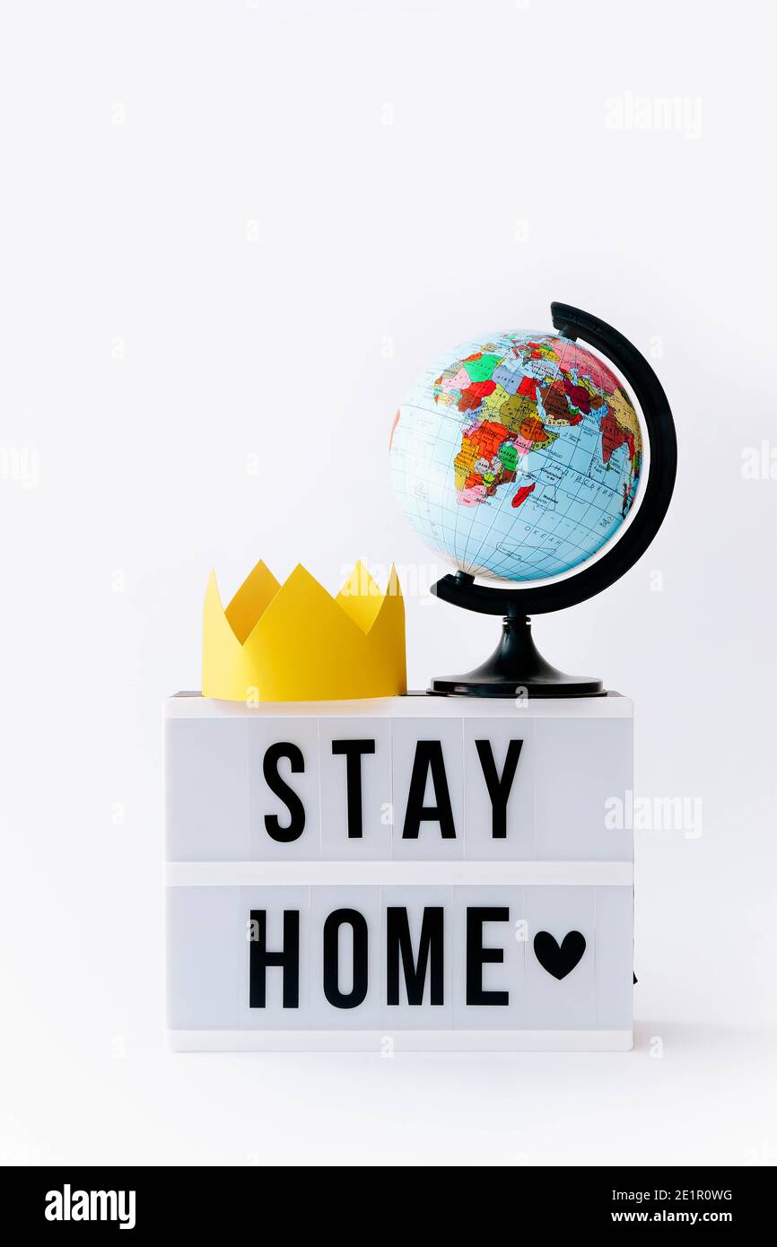 Konzept von Covid 19. Stay Home Text auf dem Display in Leuchtkasten und Globus mit Krone darauf, heller Hintergrund. Stockfoto
