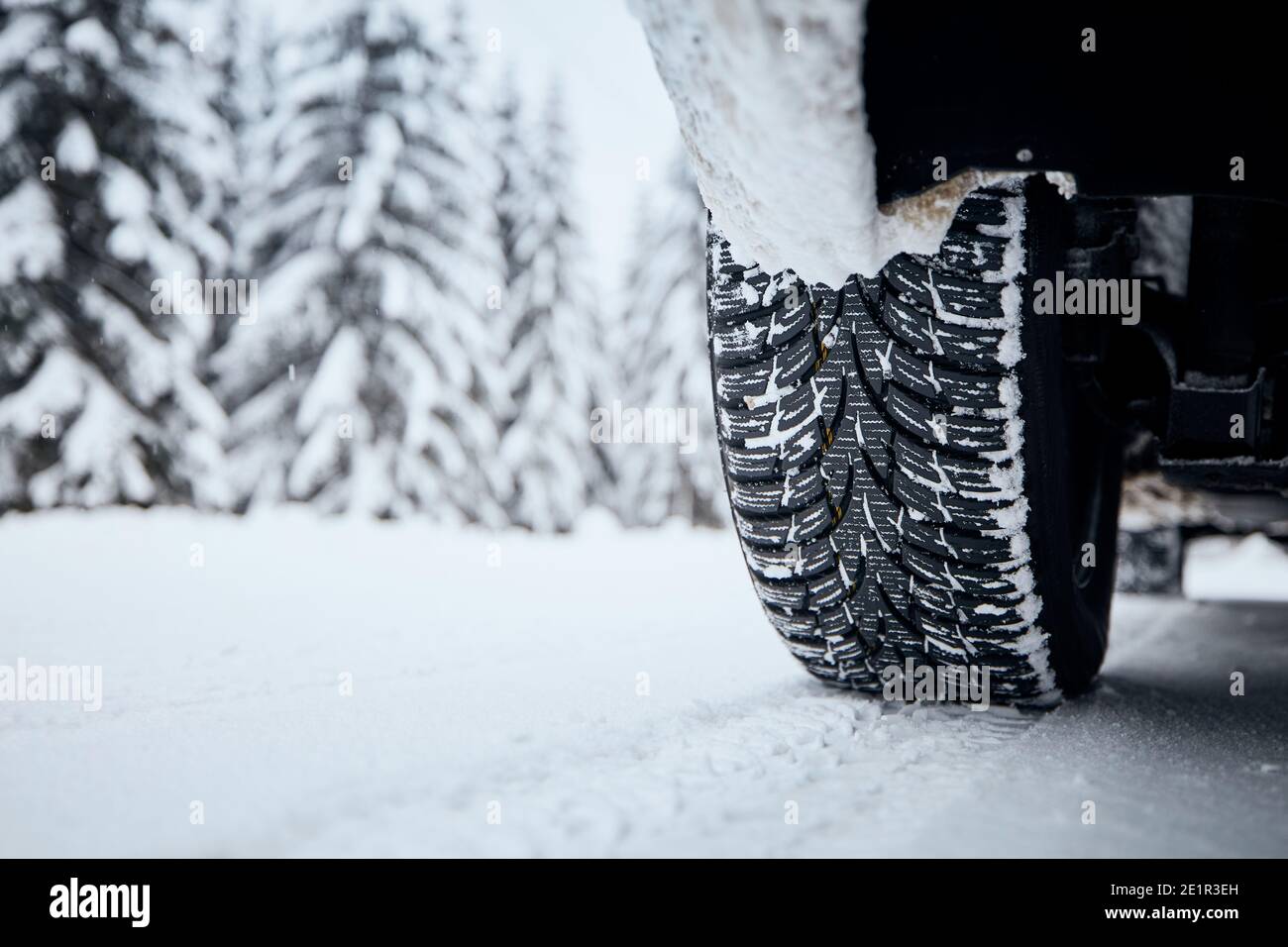 Nahaufnahme des Autoreifens auf schneebedeckter und vereister Straße. Themen Sicherheit und Fahren im Winter. Stockfoto