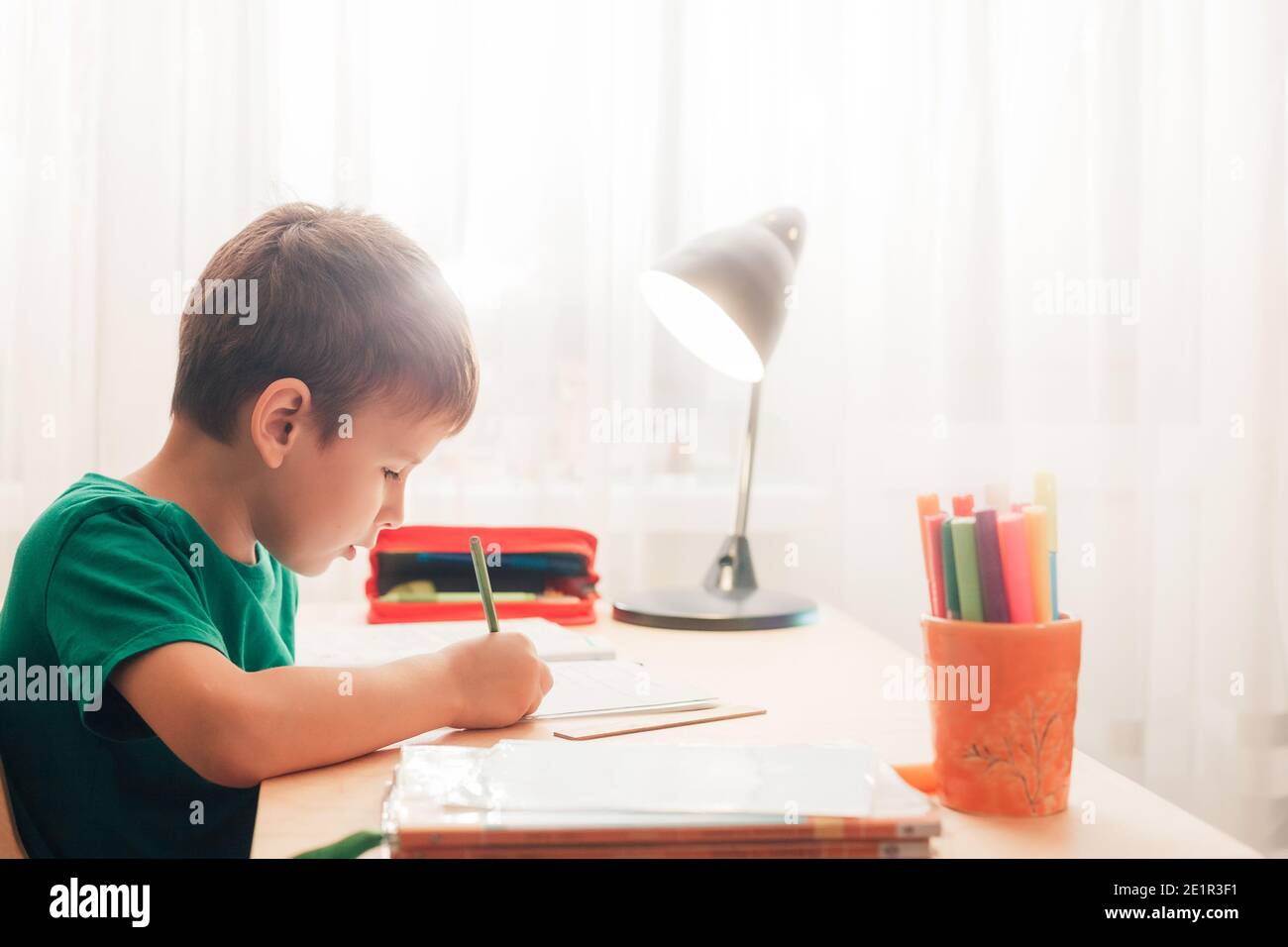 Niedlich 7 Jahre alt Kind Junge tun seine Wittling Hausaufgaben in Notebook sitzen am Schreibtisch. Seitenansicht Stockfoto