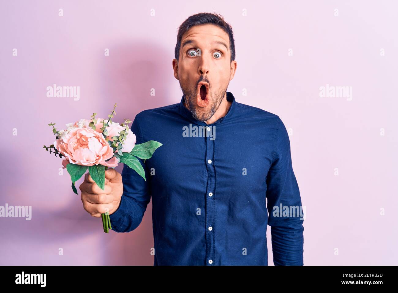 Junge gutaussehende romantischen Mann hält schöne Blumenstrauß über rosa Hintergrund verängstigt und erstaunt mit offenem Mund für Überraschung, Unglauben Gesicht Stockfoto