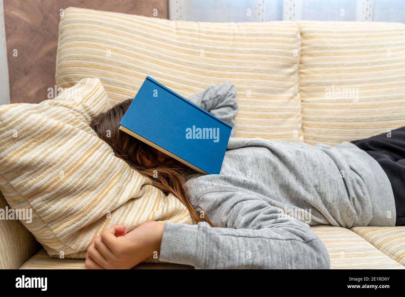 Nettes kleines Mädchen, das mit einem Buch nippt, das sie gerade auf dem Sofa in ihrem Wohnzimmer gelesen hat. Selektiver Fokus. Rest-Konzept. Stockfoto