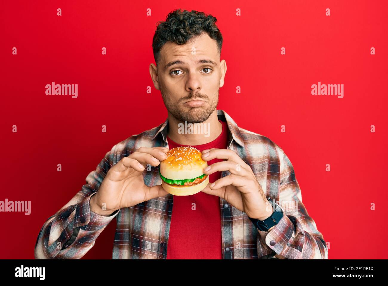 Junge hispanische Mann essen einen leckeren klassischen Burger deprimiert und sorgen für Not, Weinen wütend und Angst. Trauriger Ausdruck. Stockfoto