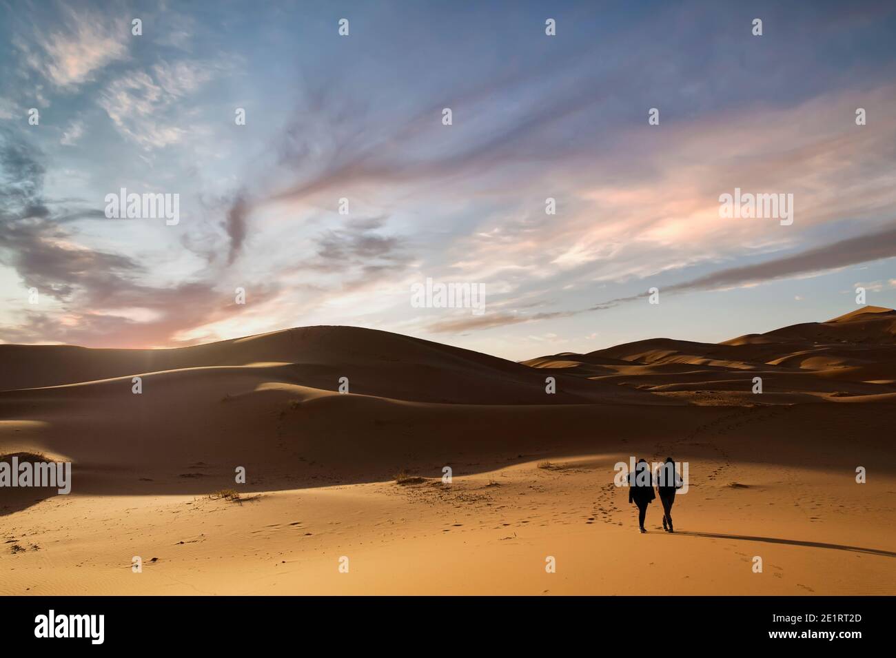 (Selektiver Fokus) Silhouette von zwei Personen, die während eines atemberaubenden Sonnenuntergangs auf den Sanddünen der Merzouga-Wüste wandern. Merzouga, Marokko. Stockfoto