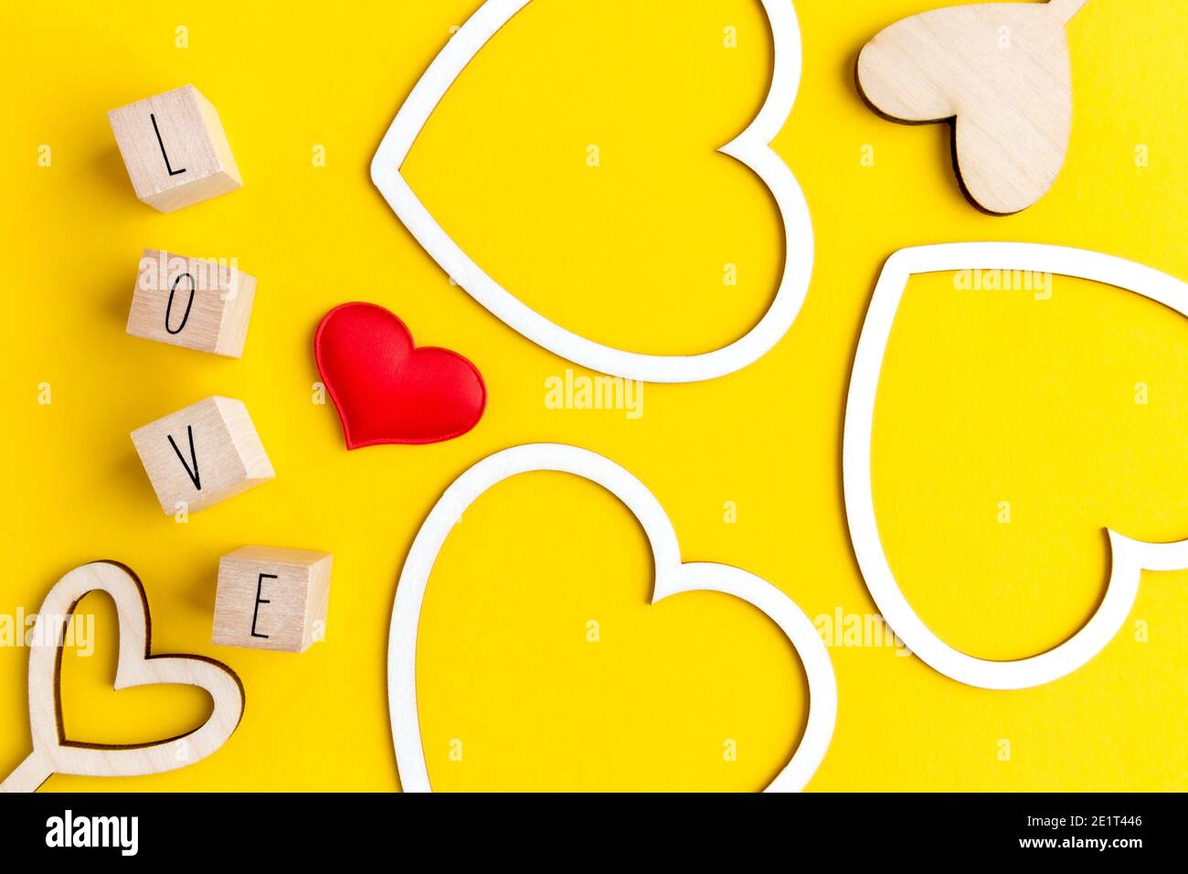 Flache Herzformen aus weißem Karton, Holz und Buchstaben mit dem Wort Liebe auf gelbem Hintergrund mit Platz für Text. Postkartenlayout für das Stockfoto