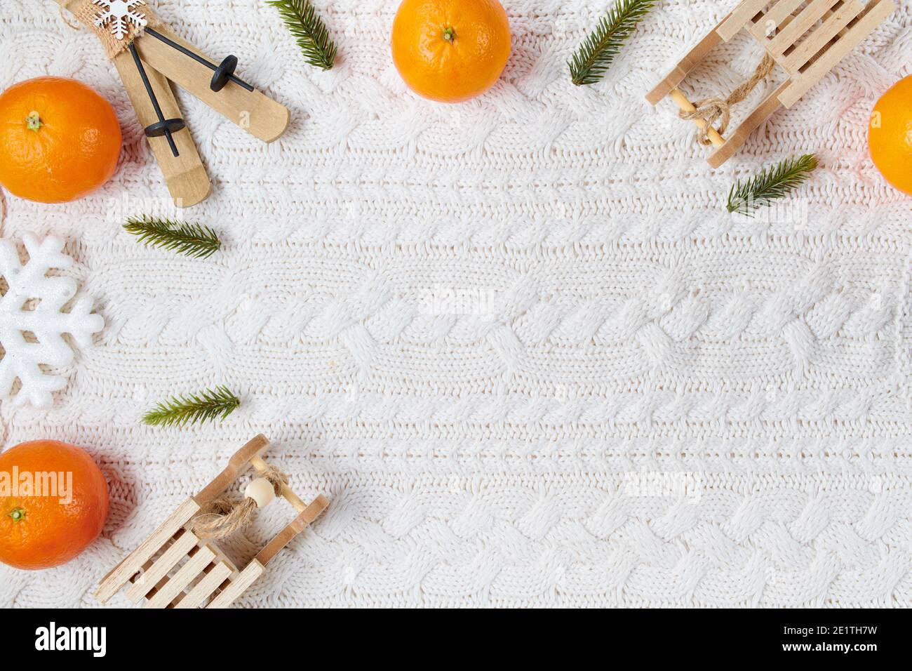 Winterflachlage mit Schneeflocken, Mandarinen, Schlitten und Skiern auf weißem Strickhintergrund. Stockfoto