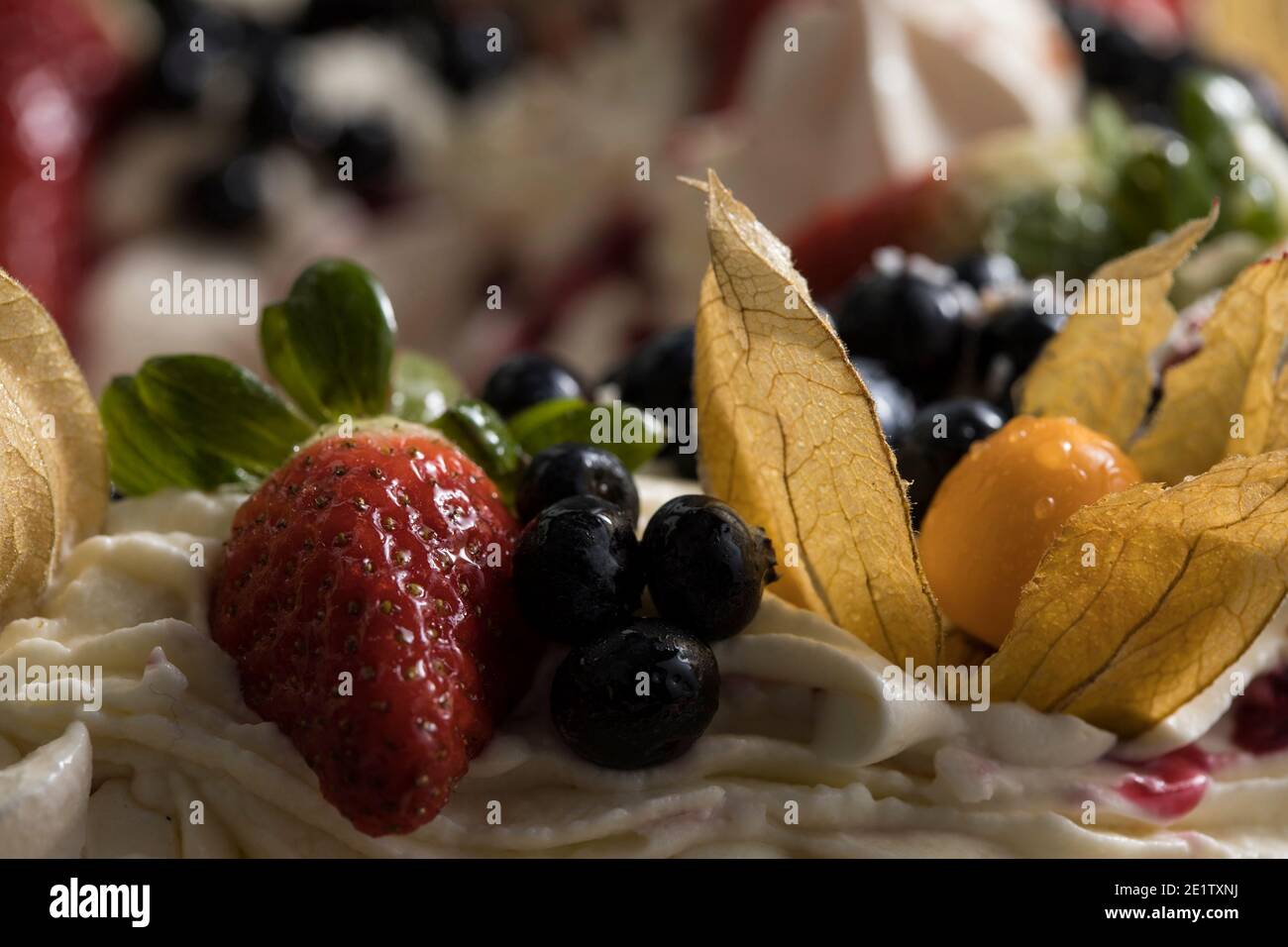 Köstlicher pavlova-Kuchenkranz aus französischer Baiser und Schlagsahne, verziert mit Erdbeere, Blaubeeren und Physalis Stockfoto