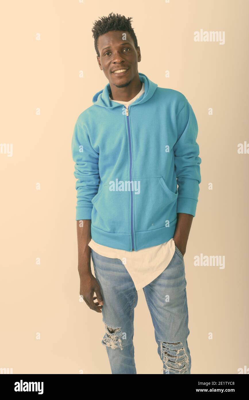 Studio shot der jungen schwarzen afrikanischen Mann glücklich lächelnd und stand mit der Hand in der Tasche vor weißem Hintergrund Stockfoto