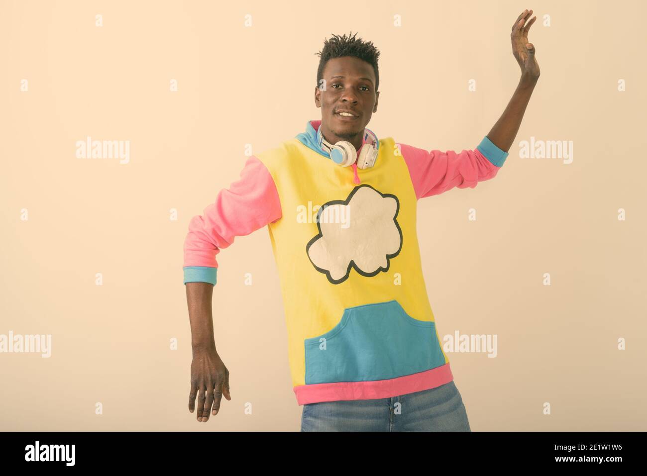 Studio shot von jungen schwarzen afrikanischen Mann, lustige Gesten mit beiden Händen beim Tragen der Kopfhörer um den Hals vor weißem Hintergrund Stockfoto