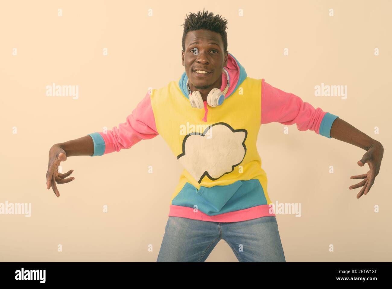 Studioaufnahme des jungen glücklichen schwarzen afrikanischen Mannes lächelnd während Mit beiden Händen lustige Gesten machen und Kopfhörer tragen Hals gegen Weiß Stockfoto