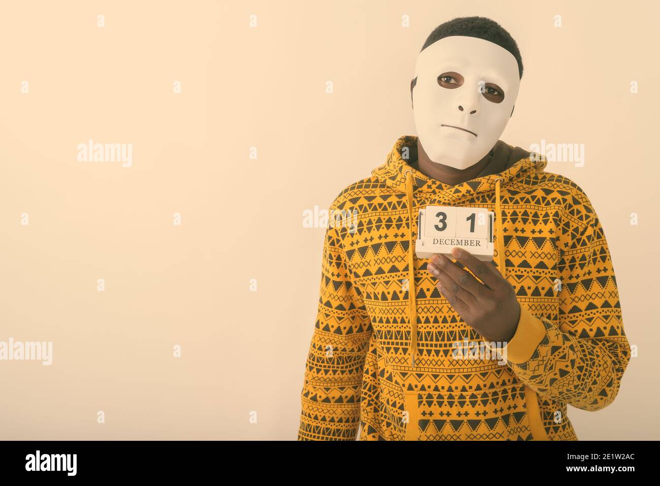 Studio shot von jungen schwarzen afrikanischen Mann, weiße Maske, während sie zum 31. Dezember Kalender vor weißem Hintergrund Stockfoto