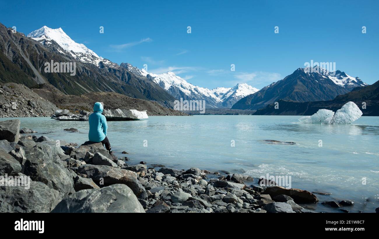 Touristen sitzen am Ufer des Tasman Glacier Terminal Lake Blick auf schneebedeckte Berge und Eisberge Stockfoto