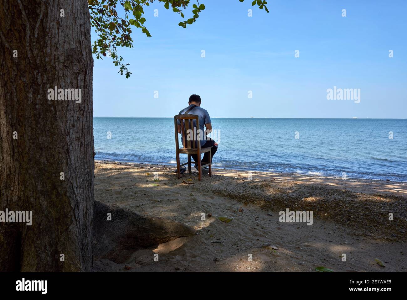 Einsamer Mann sitzt auf einem Stuhl und entspannt sich im Freien Strand und Blick auf das Meer in Thailand Südostasien Stockfoto