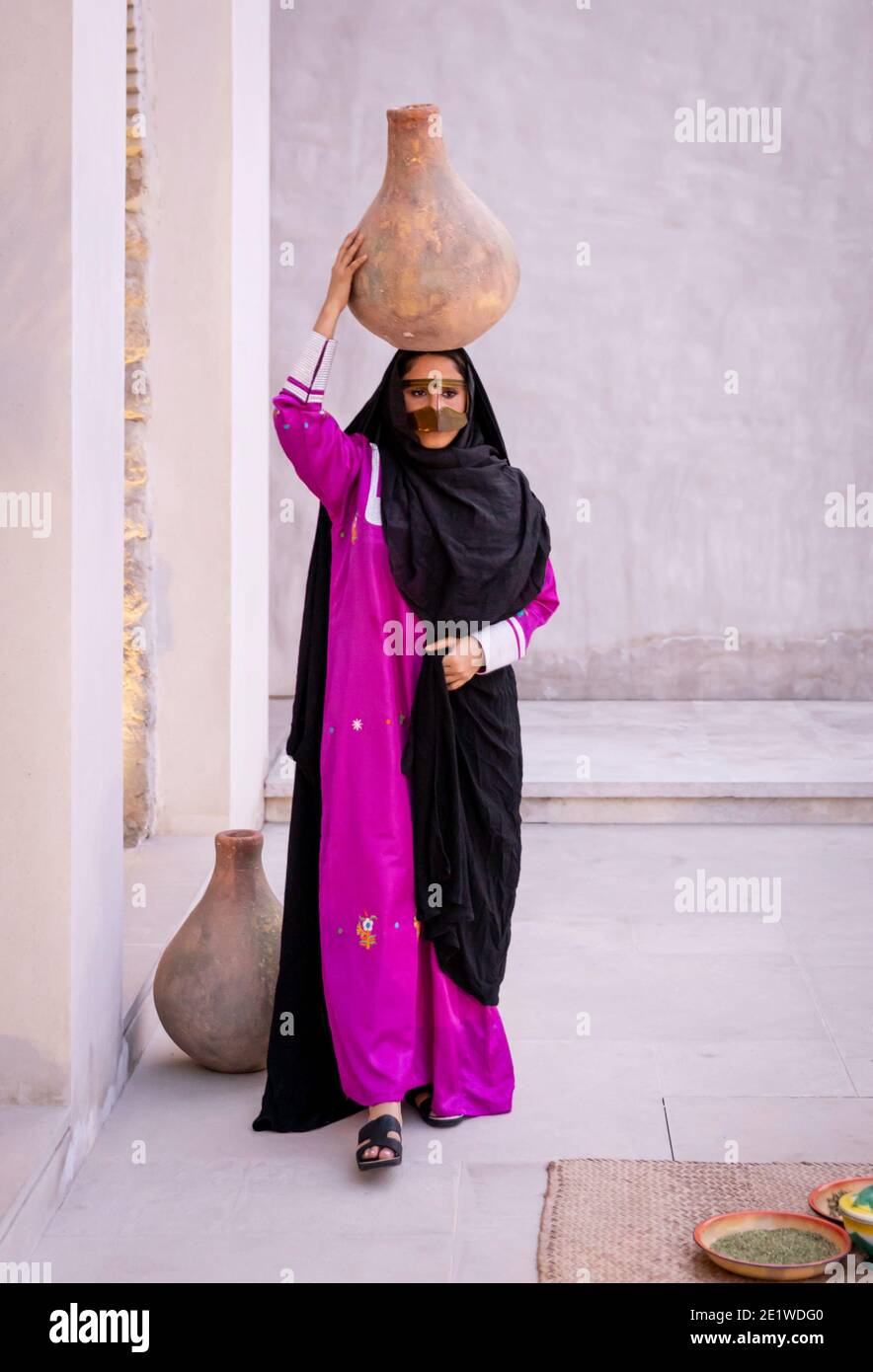 Emarati Dame in traditionellen Kleidern hält ein Glas über ihr Kopf und Roaming rund um das Haus Stockfoto