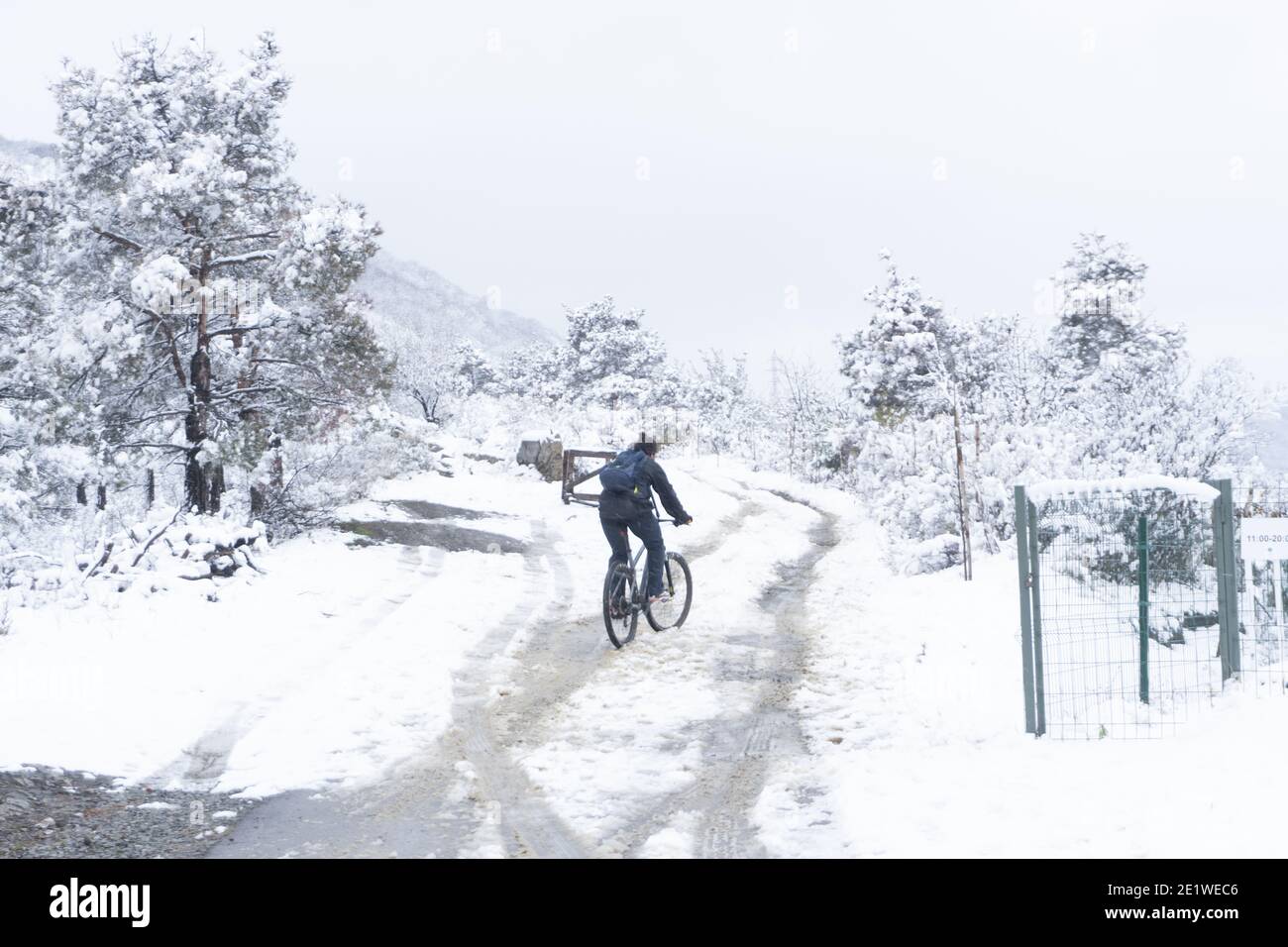 Ein junger Mann versucht, auf einer schneebedeckten Bergstraße mit dem Fahrrad zu fahren. Klimawandel in einem warmen Land, eine unerwartete Katastrophe. Stockfoto