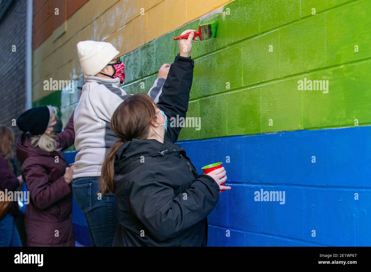 Community-Mitglieder malen ein Wandbild neu, das mit weißen nationalistischen Graffiti verunstaltet wurde.Dutzende von Community-Mitgliedern versammelten sich bei Jake's Cards and Games, um das defaced Pride-Wandbild auf der Seite des Unternehmens neu zu malen. Freiwillige wechselten sich ab, um die sprühgemalten Botschaften der weißen nationalistischen Gruppe Patriot Front zu übermalen. Stockfoto