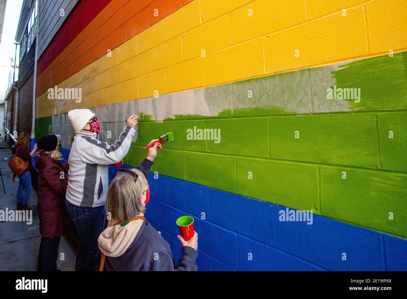 Community-Mitglieder malen ein Wandbild neu, das mit weißen nationalistischen Graffiti verunstaltet wurde.Dutzende von Community-Mitgliedern versammelten sich bei Jake's Cards and Games, um das defaced Pride-Wandbild auf der Seite des Unternehmens neu zu malen. Freiwillige wechselten sich ab, um die sprühgemalten Botschaften der weißen nationalistischen Gruppe Patriot Front zu übermalen. Stockfoto