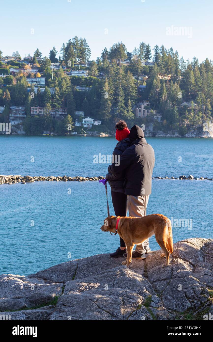 Rückansicht des jungen Mannes und der Frau steht auf einer felsigen Klippe, die sich und ihren Hund neben sich umarmt. Kalter Herbsttag. Selektiver Fokus, trav Stockfoto