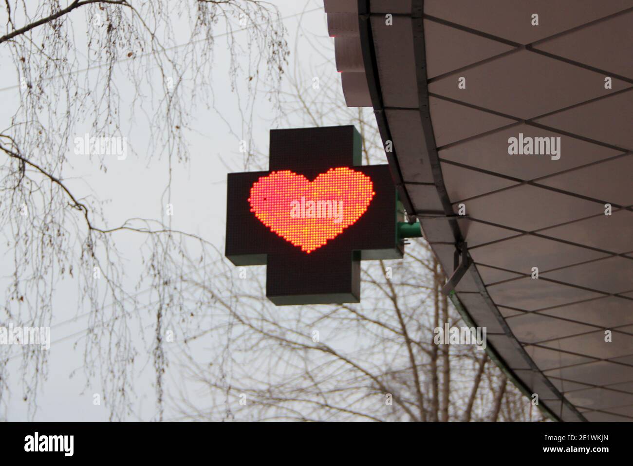 Rotes Herz auf einer Lichttafel in Form eines Kreuzes. Werbegestaltung einer Apotheke auf einer Stadtstraße. Stockfoto