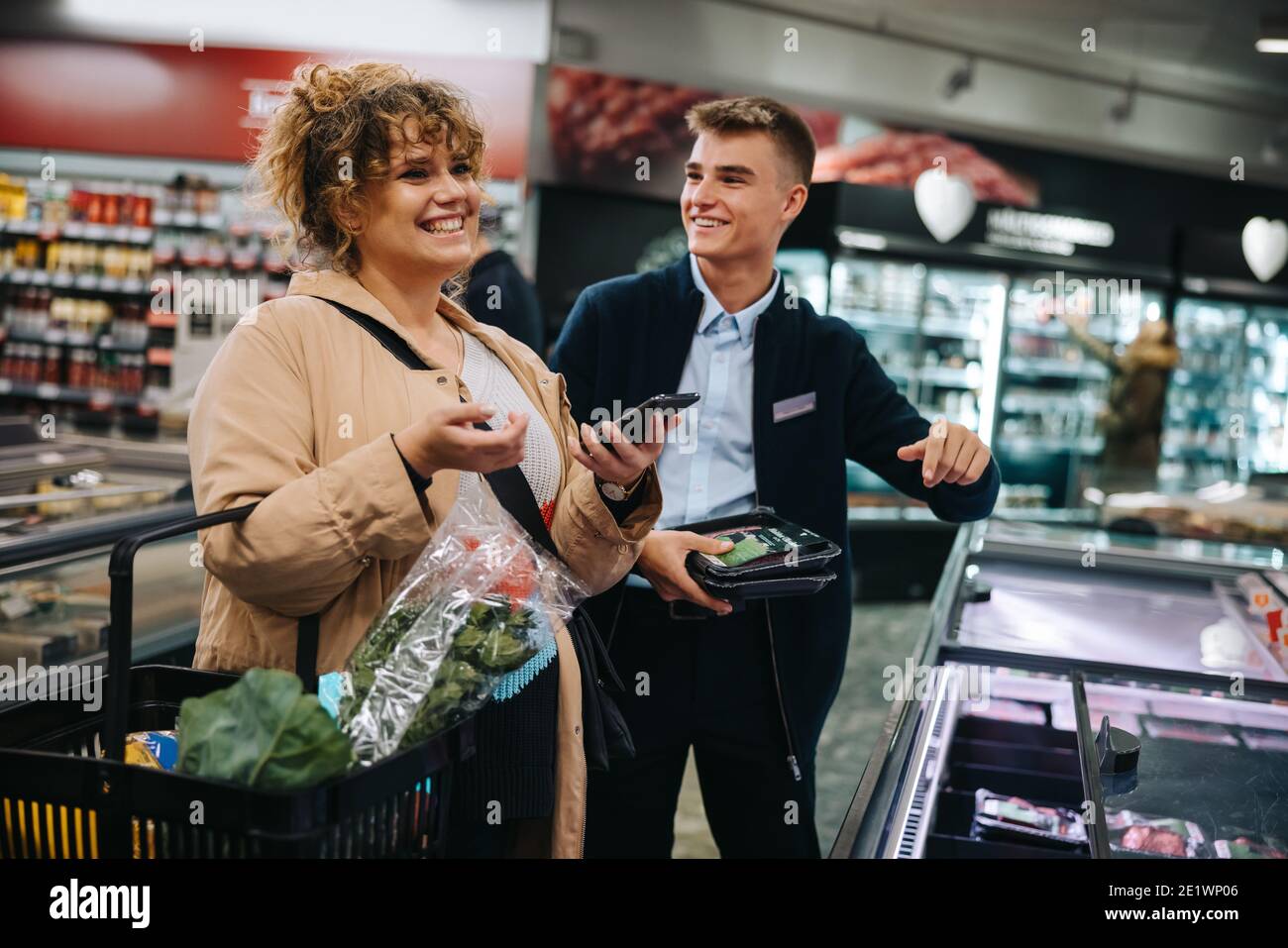 Lächelnde weibliche Shopper mit Assistent im Lebensmittelgeschäft. Glückliche Frau Kunde einkaufen im Supermarkt. Stockfoto