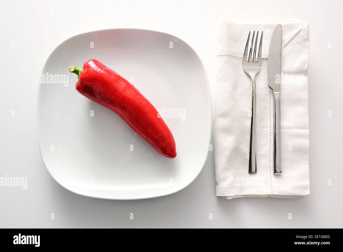 Roher roter, spitzer Paprika auf weißem Teller, Besteck und Serviette daneben auf hellem Hintergrund, gesunde Ernährung mit Gemüse oder Diät, um Gewicht zu verlieren Stockfoto