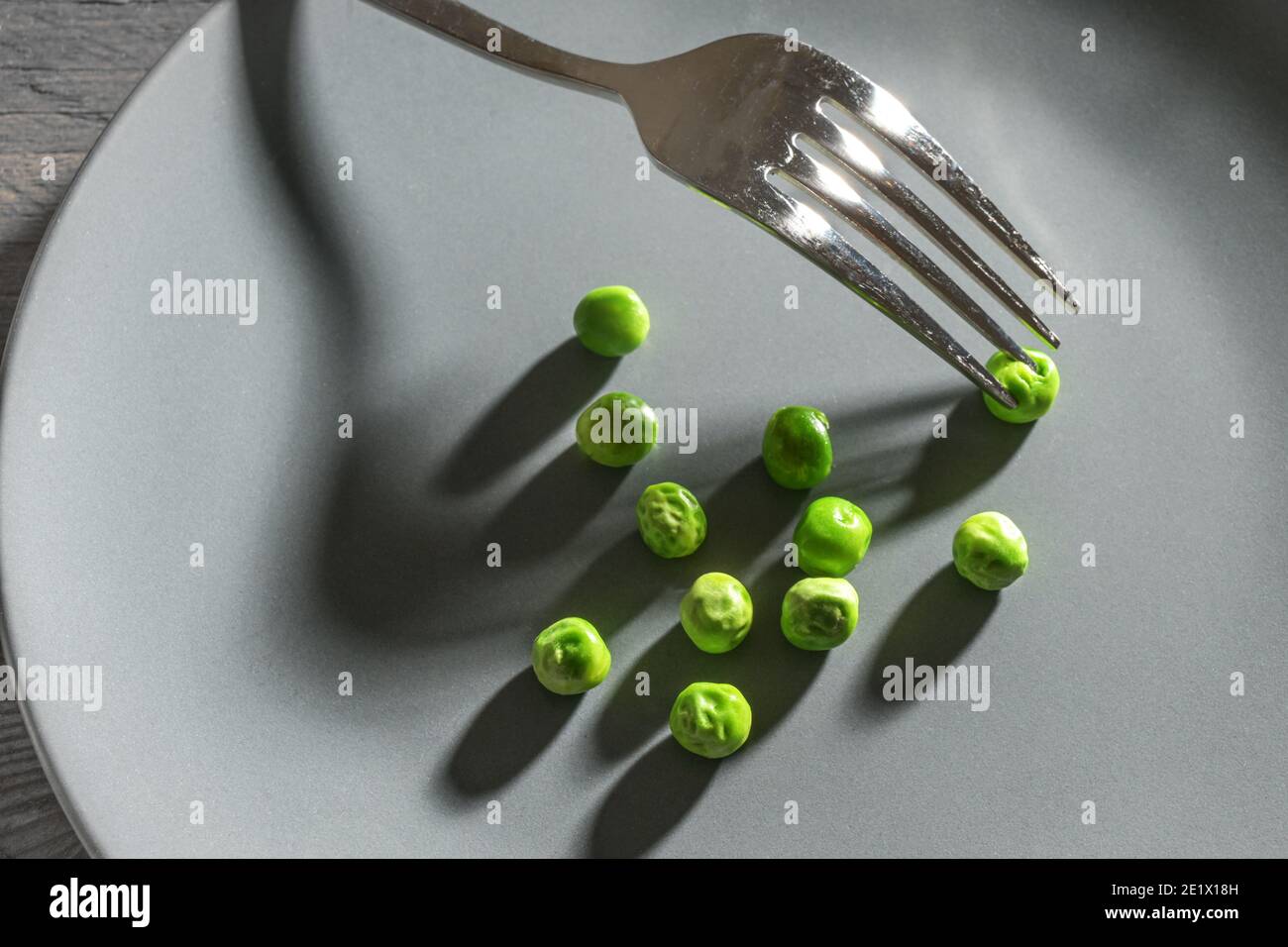 Einige grüne Erbsen und eine Gabel mit Schatten auf einem grauen Teller, magere Ernährung Mahlzeit nach der Auflösung zu schlank, Kopierer Raum, ausgewählten Fokus Stockfoto
