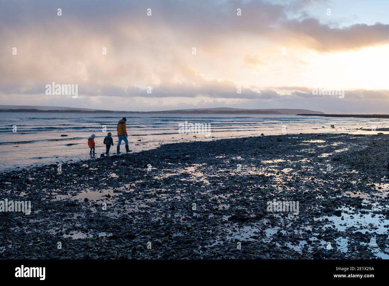 Vater mit seinen beiden kleinen Kindern zu Fuß entlang der Küste in Lepe im Winter, Hampshire, England Stockfoto